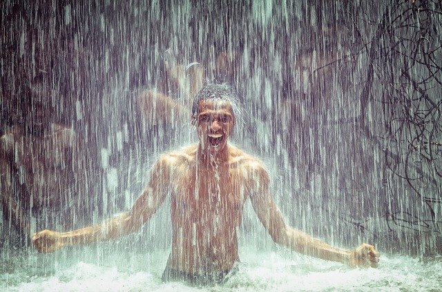 homme souriant torse nu sous cascade d'eau